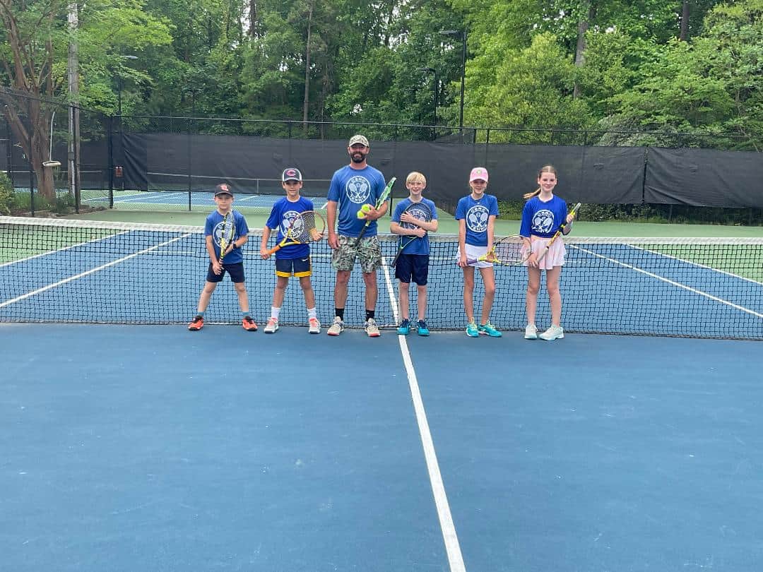 Adam Maskill on the tennis court with 5 young campers.